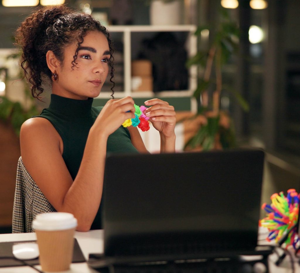 A young woman with dark brown textured here is using a fidget toy while working in the office