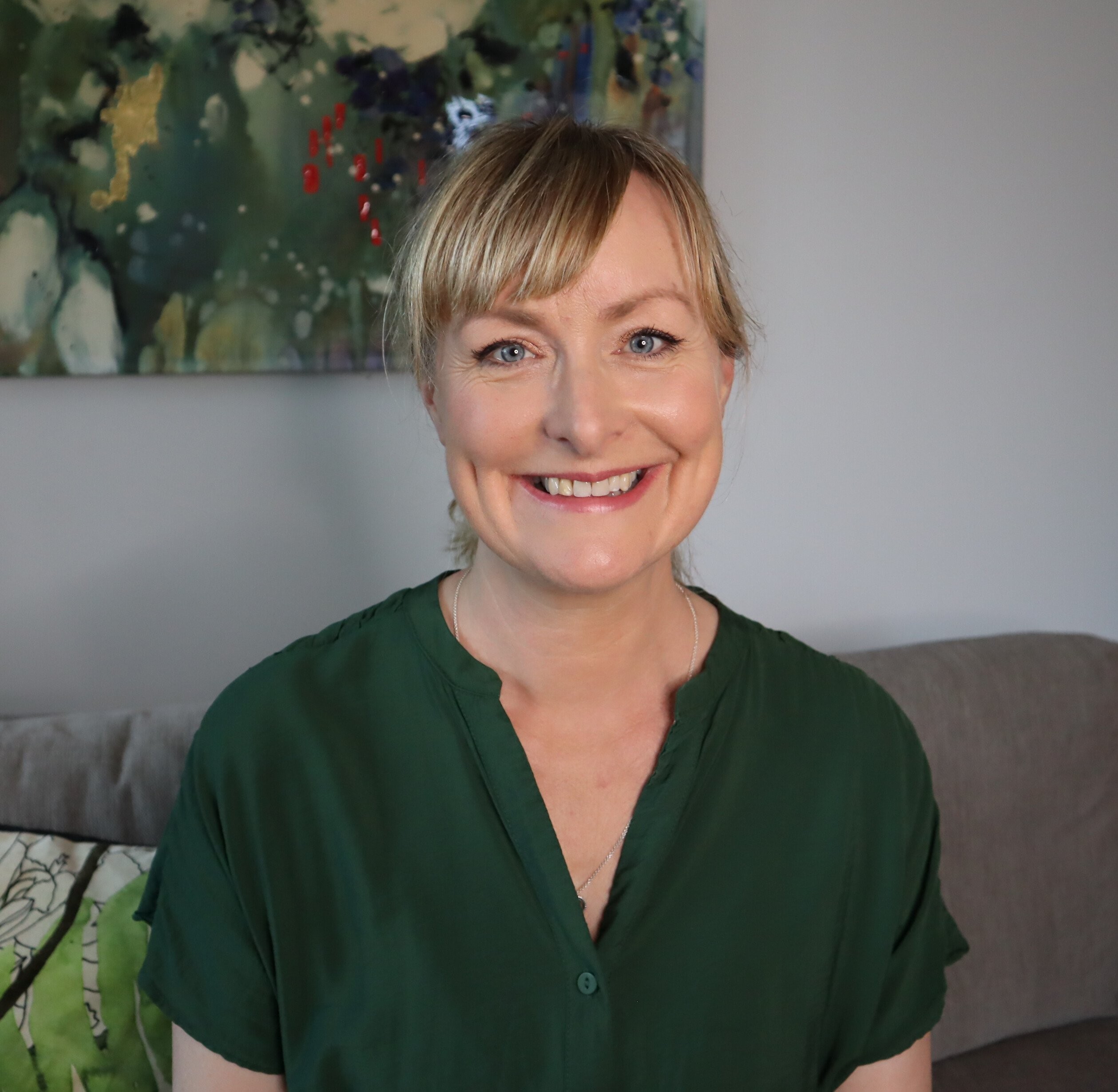 Jane is a white woman with dark blonde hair and blue eyes. She is wearing a dark green shirt and is smiling into the camera.