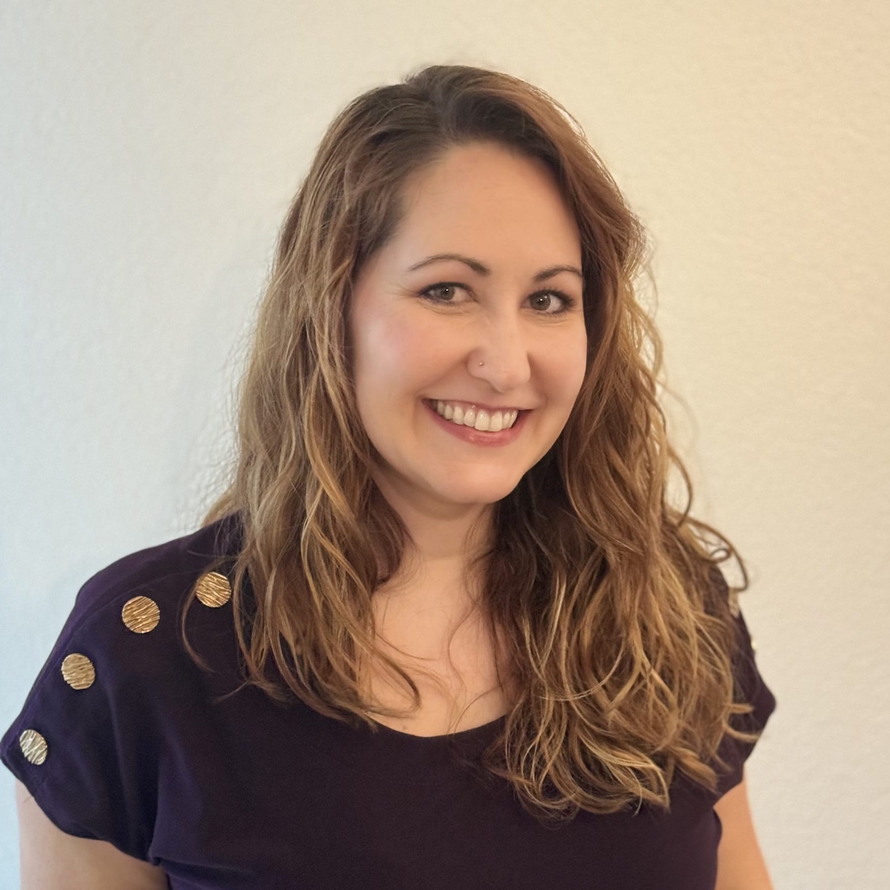 Samantha is a white woman with mid-length wavy light brown hair and hazel eyes. She has a warm smile and she wears a dark purple blouse.