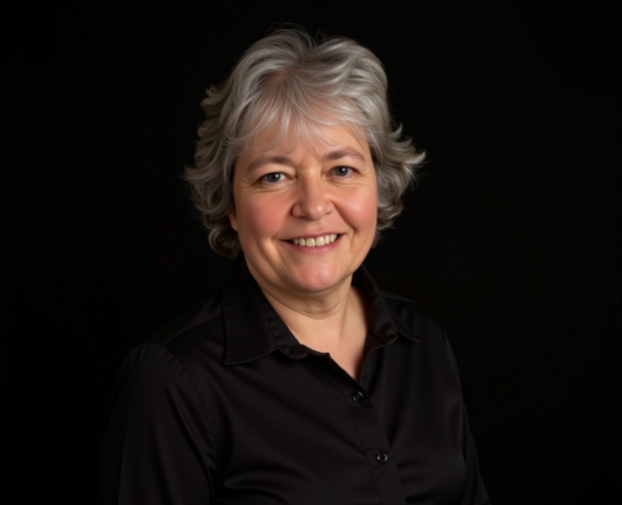 Susan is a white woman with short, wavy silver hair. She is wearing a black button-up shirt, adding to the professional yet friendly appearance.